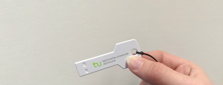 Hand hält einen Plastikschlüssel mit dem TU-Logo