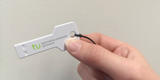 A hand holds a plastic key with TU logo