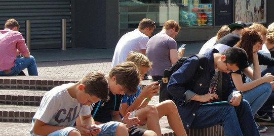 TU App Studenten auf dem Campus schauen auf ihr Smartphone. Rechts auf dem Bild sind Icons der TU App eingeblendet.