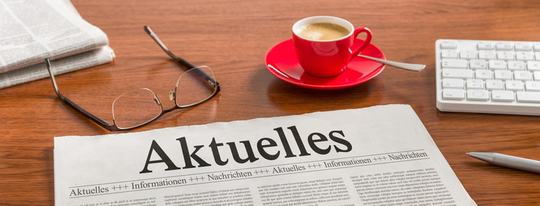 Tageszeitung mit Titel Aktuelles Brille, Kaffeetasse und Tageszeitung mit Titel Aktuelles auf einem Tisch