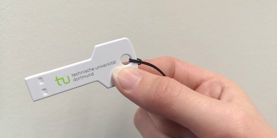 Softwareschlüssel Eine Hand hält einen Plastikschlüssel mit TU-Logo