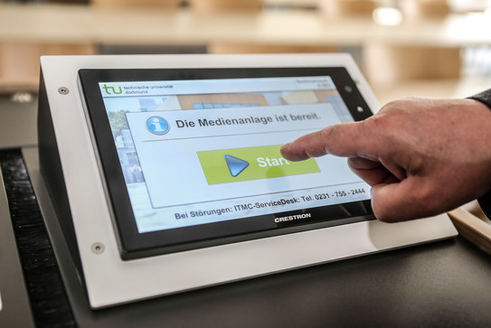 Hörsaalpult Eine Person tippt mit einem Finger auf einem Bildschirm am Hörsaalpult.
